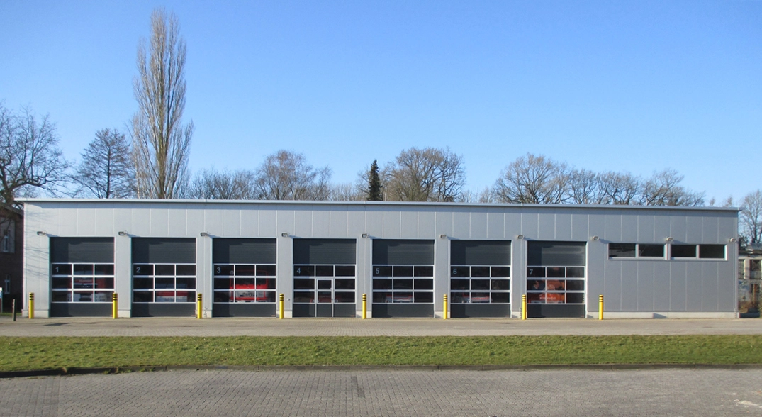 Graues Gebäude mit sieben Garagentoren, umgeben von Bäumen und Himmel, Feuerwehr Haarentor