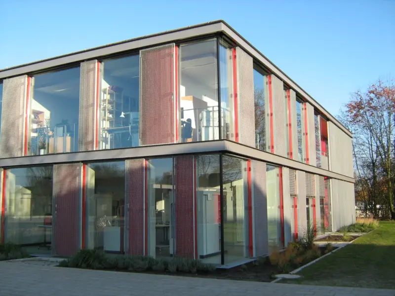 Modernes Gebäude mit Glasfassade und rotem Akzentstreifen, umgeben von Bäumen. Name der Schule: LSG Gymnasium Rahmsloh