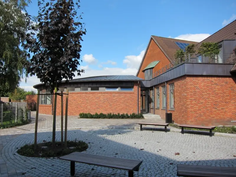 Backsteinfassade der St. Willehad Kirche mit gepflastertem Vorplatz und Bänken unter blauem Himmel